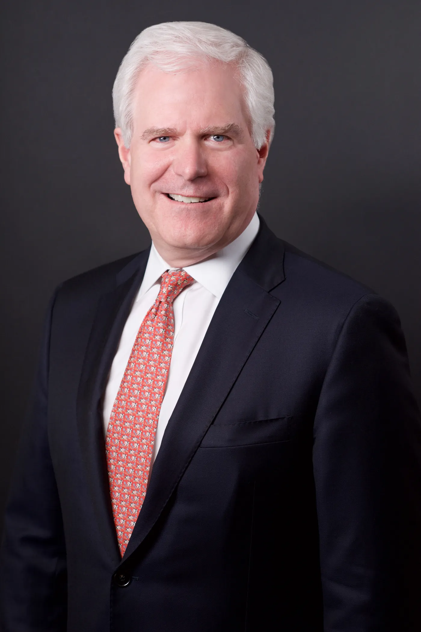 Senior executive business headshot, white hair, red tie, charcoal backdrop