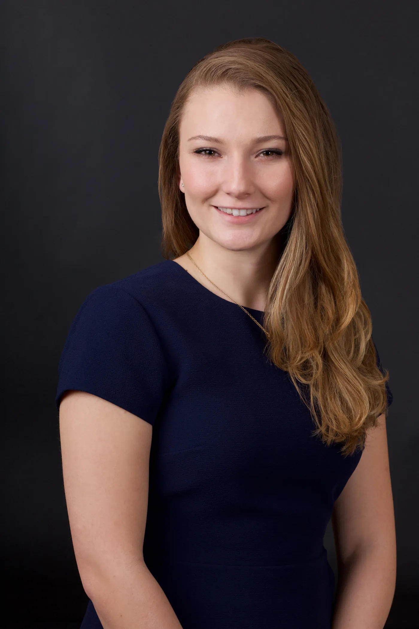 Professional headshot of a woman with long hair in a navy dress