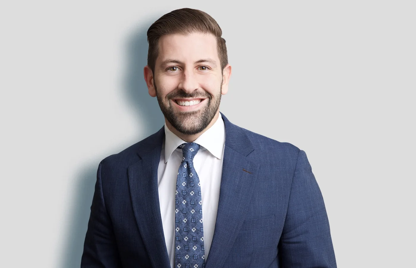 Team headshot of a smiling man in a blue suit on a light gray backdrop