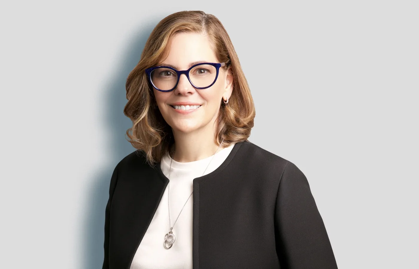 Team headshot of a woman in glasses on a light gray backdrop